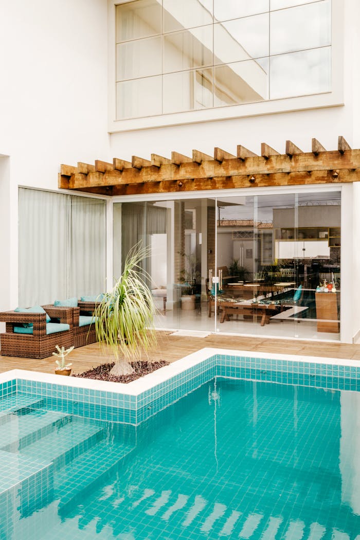 Stylish outdoor patio featuring a pool and modern architecture with glass doors and wooden pergola.